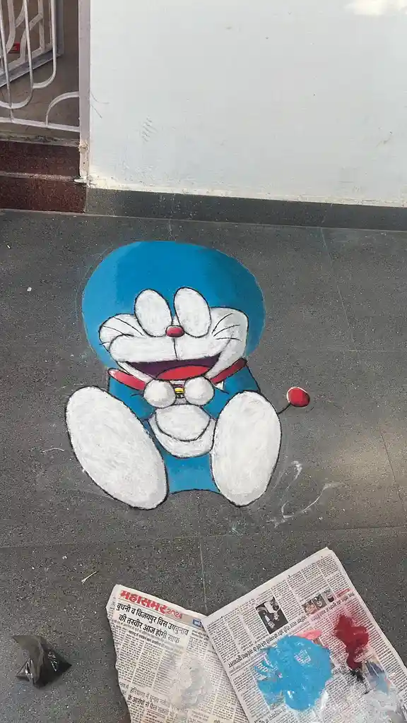 A chalk drawing of the cartoon character Doraemon is on a dark tiled floor, with a newspaper spread nearby showing smudged…