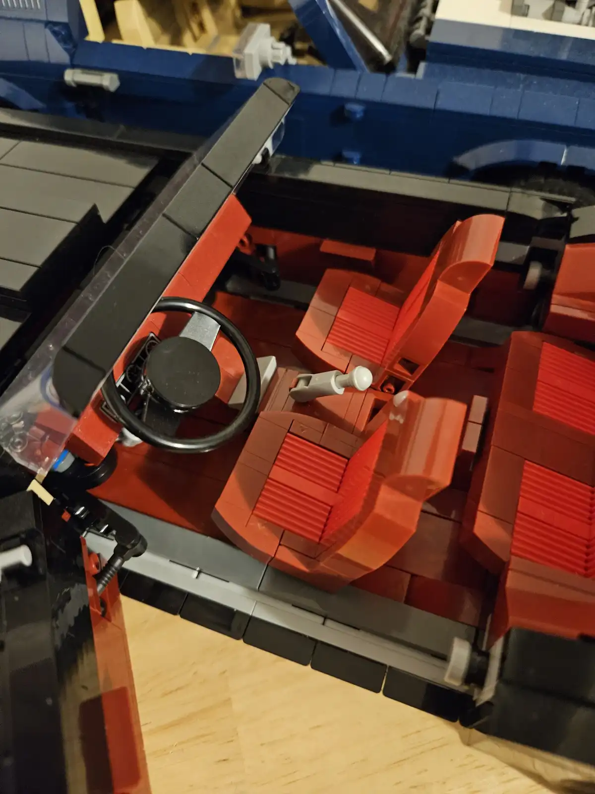 A close-up shot of the interior of a detailed Lego car model, showing red seats, a black steering wheel, and grey dashboard…