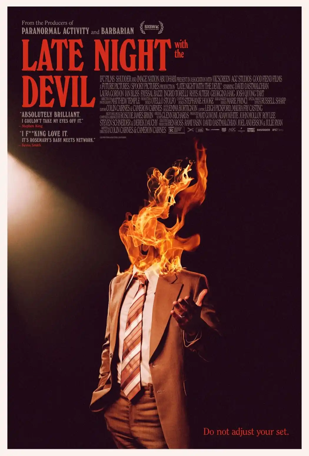 A movie poster for 'Late Night with the Devil' shows a man in a suit and tie with his head engulfed in flames, under a…
