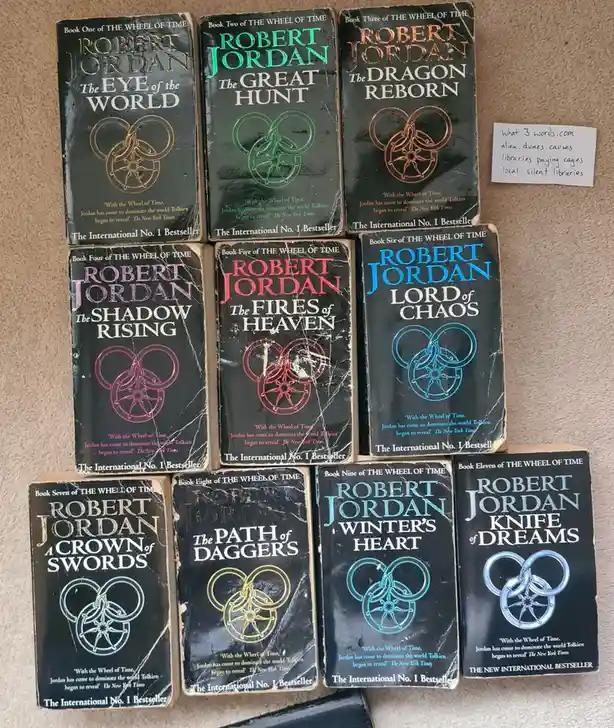 Nine worn paperback books from Robert Jordan's 'The Wheel of Time' series are arranged on a carpeted floor, each showing its…