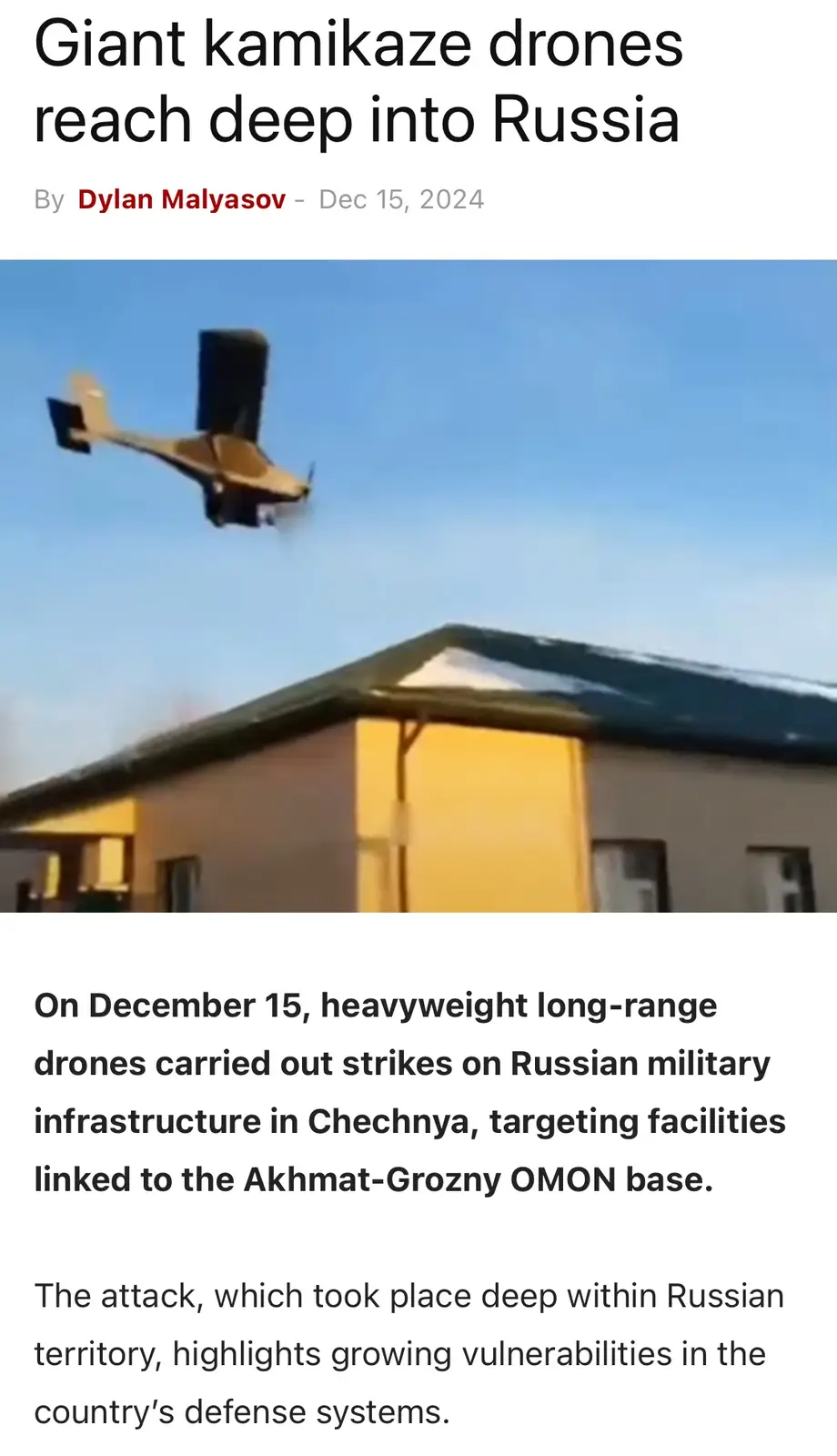 The image displays a small, single-engine drone flying low over a building with a dark roof and yellow walls under a clear…