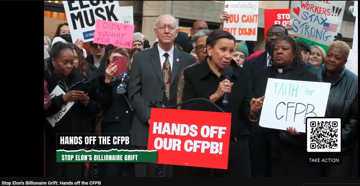 A protest scene with multiple people holding signs, including one prominently reading 'HANDS OFF OUR CFPB!' and another…
