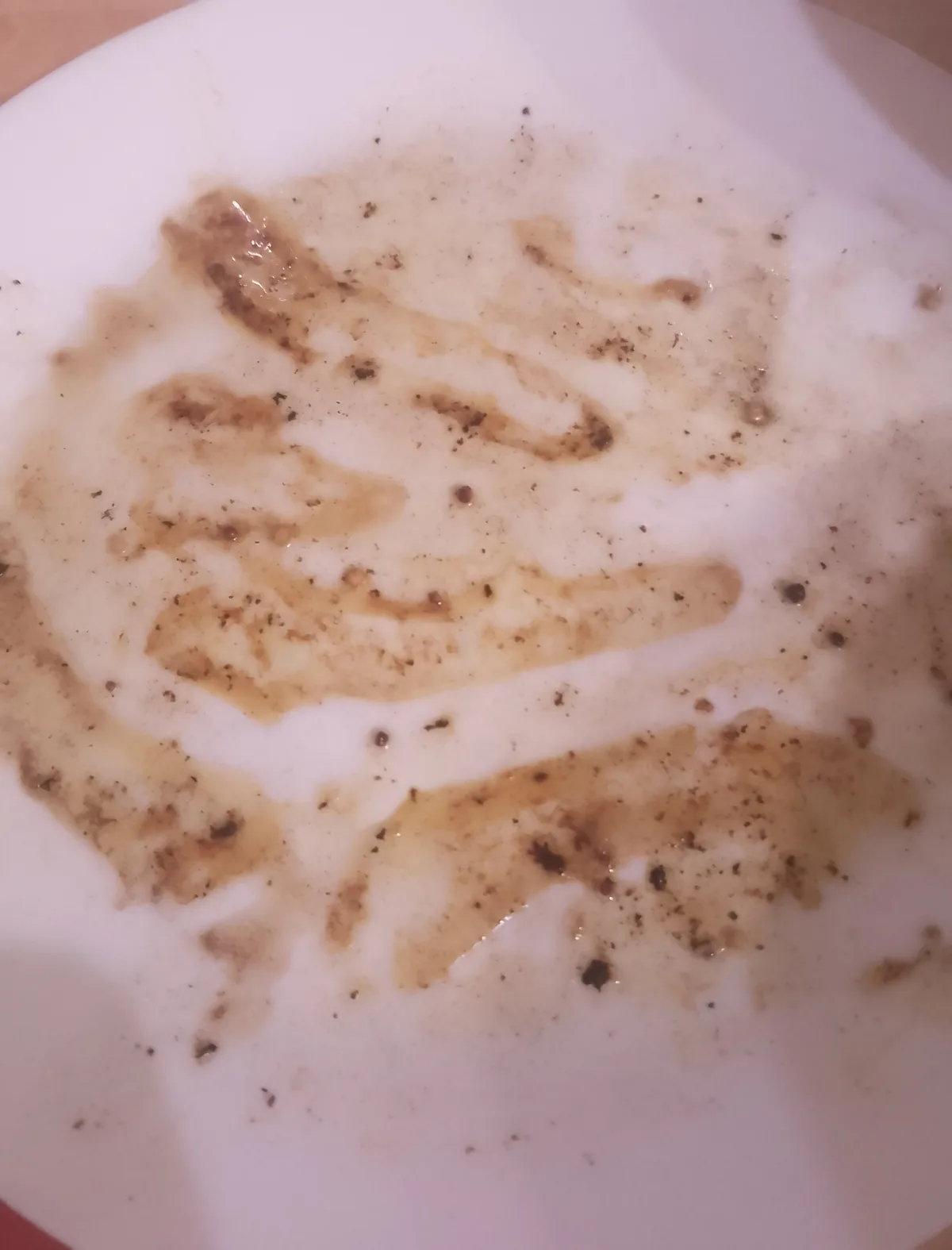 A close-up of a white plate with brown sauce and pepper residue smeared across its surface, resembling a messy eating…