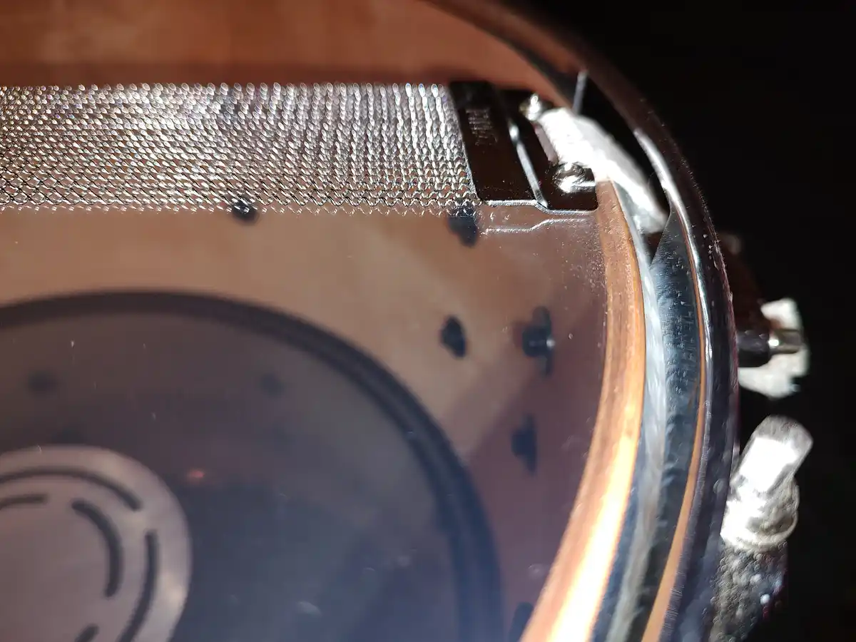 A close-up photo of a drum's hardware, showing a shiny metal mesh drumhead, chrome rim, and tension rods against a dark…