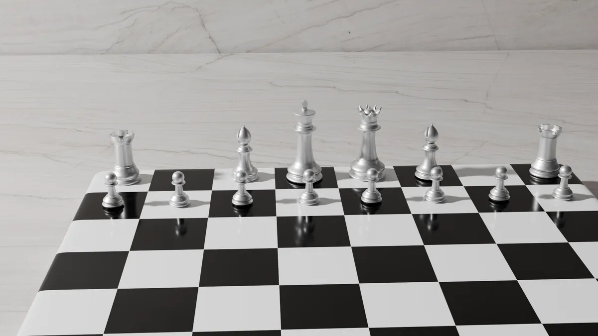 A chessboard with silver-colored pieces arranged in a starting position, viewed from a low angle on a marble surface. The…