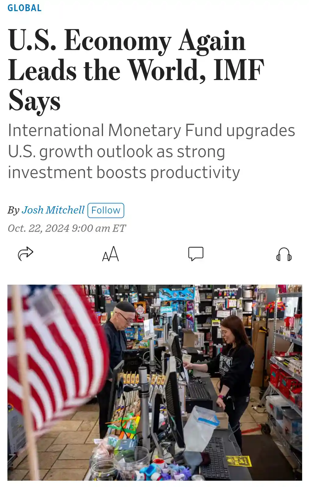 A news article headline about the U.S. economy leading the world is overlaid on a photo of a retail checkout counter where a…