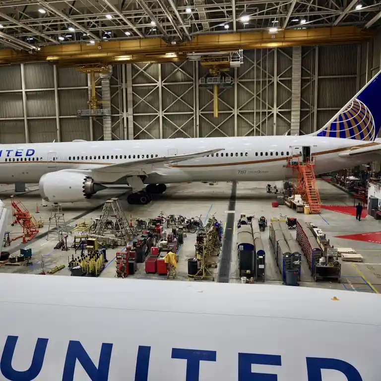 An overhead view inside a large aircraft hangar shows a United Airlines Boeing 787 Dreamliner undergoing maintenance. The…