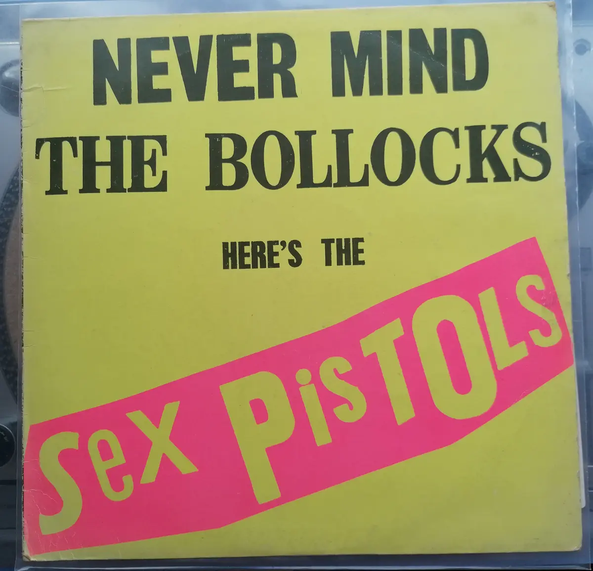The image shows the iconic yellow album cover of the Sex Pistols' debut album, featuring bold black text at the top reading…