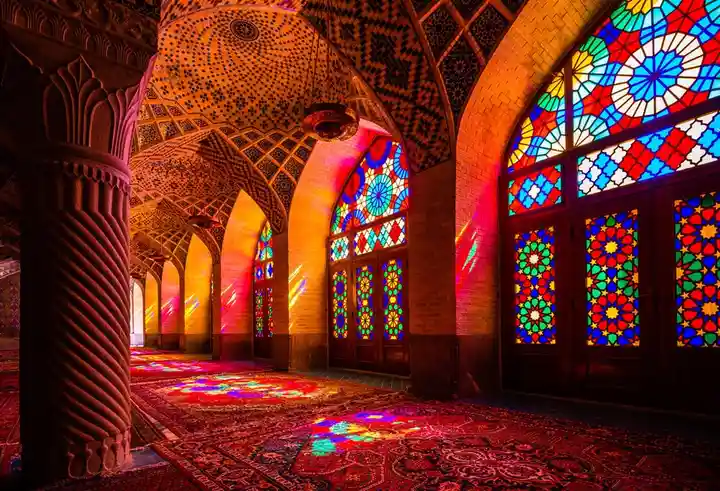 A stunning interior shot of an ornate Islamic architectural space with intricate arched ceilings, carved columns, and…
