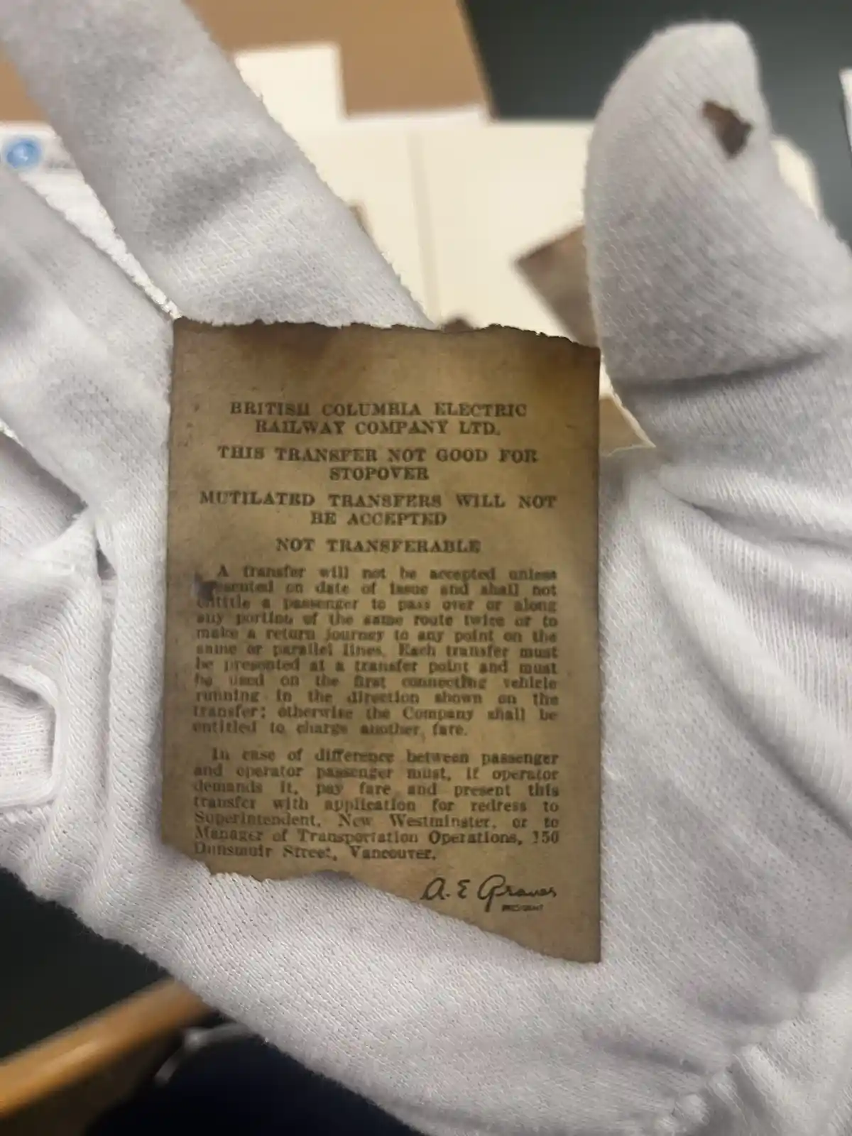 A pair of white gloves holds a torn, aged paper railway transfer from the British Columbia Electric Railway Company Ltd. The…