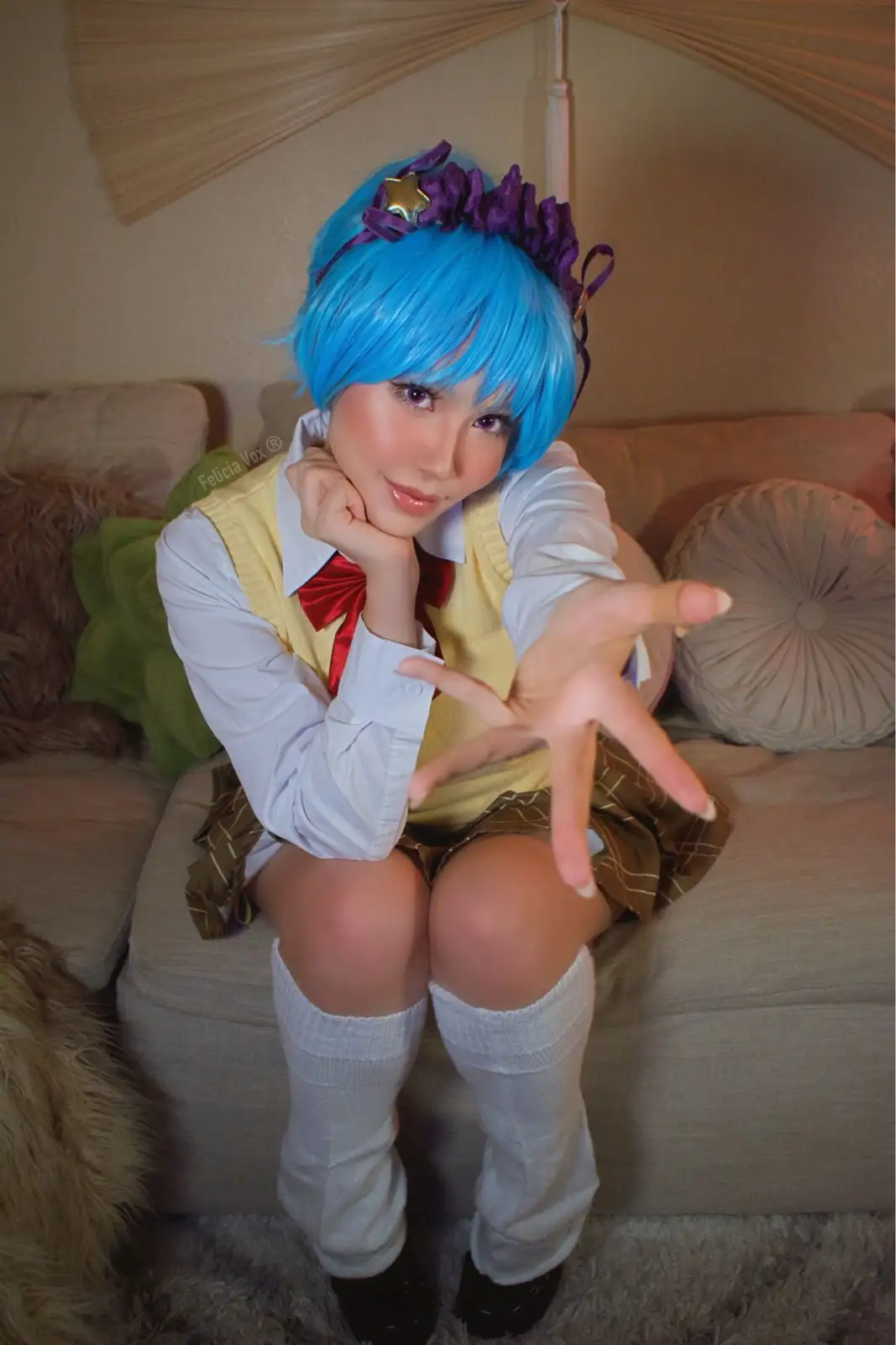 A person in a cosplay outfit with bright blue hair, a purple headband with a star, and a school uniform-style outfit sits on…