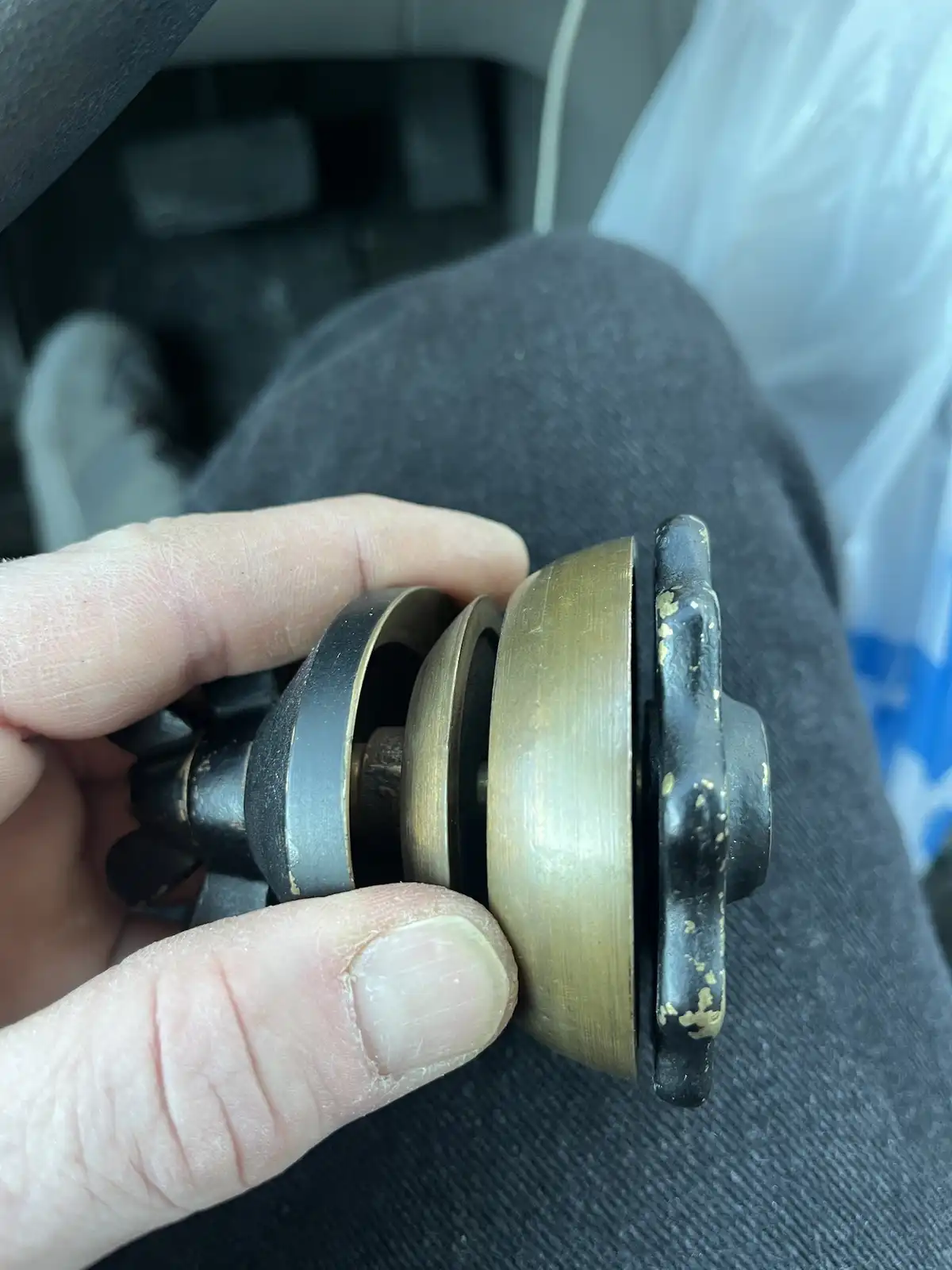 A hand holds a worn, brass-and-black mechanical object, possibly a vintage doorbell or buzzer, against a backdrop of a…