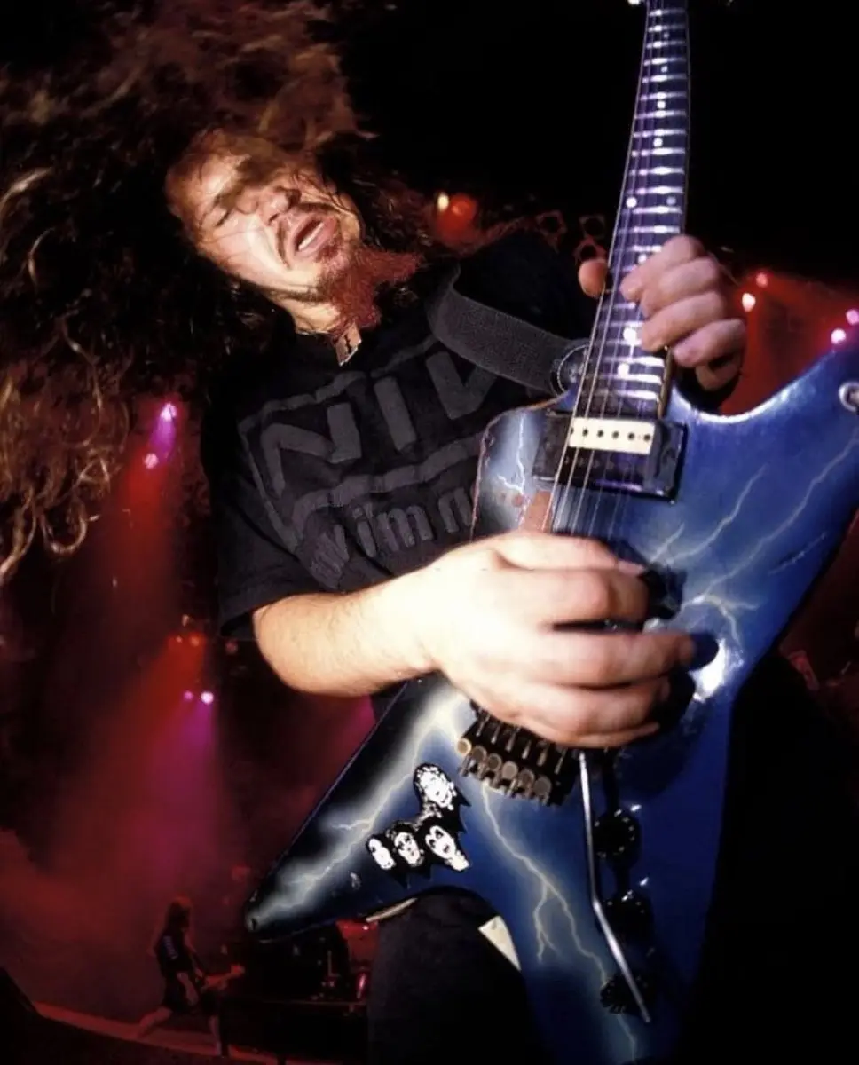 A man with long curly hair and a beard is intensely playing a blue electric guitar with lightning bolt designs on it during…