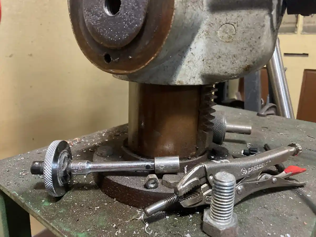 A close-up photo of a workshop bench with a large, rusty industrial machine, a crescent wrench, a socket wrench, and metal…