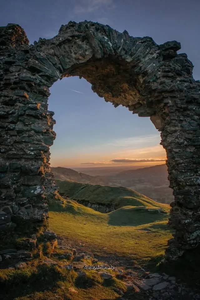 A scenic photo shows a weathered stone archway framing a beautiful sunset over rolling green hills. The overlaid text reads…