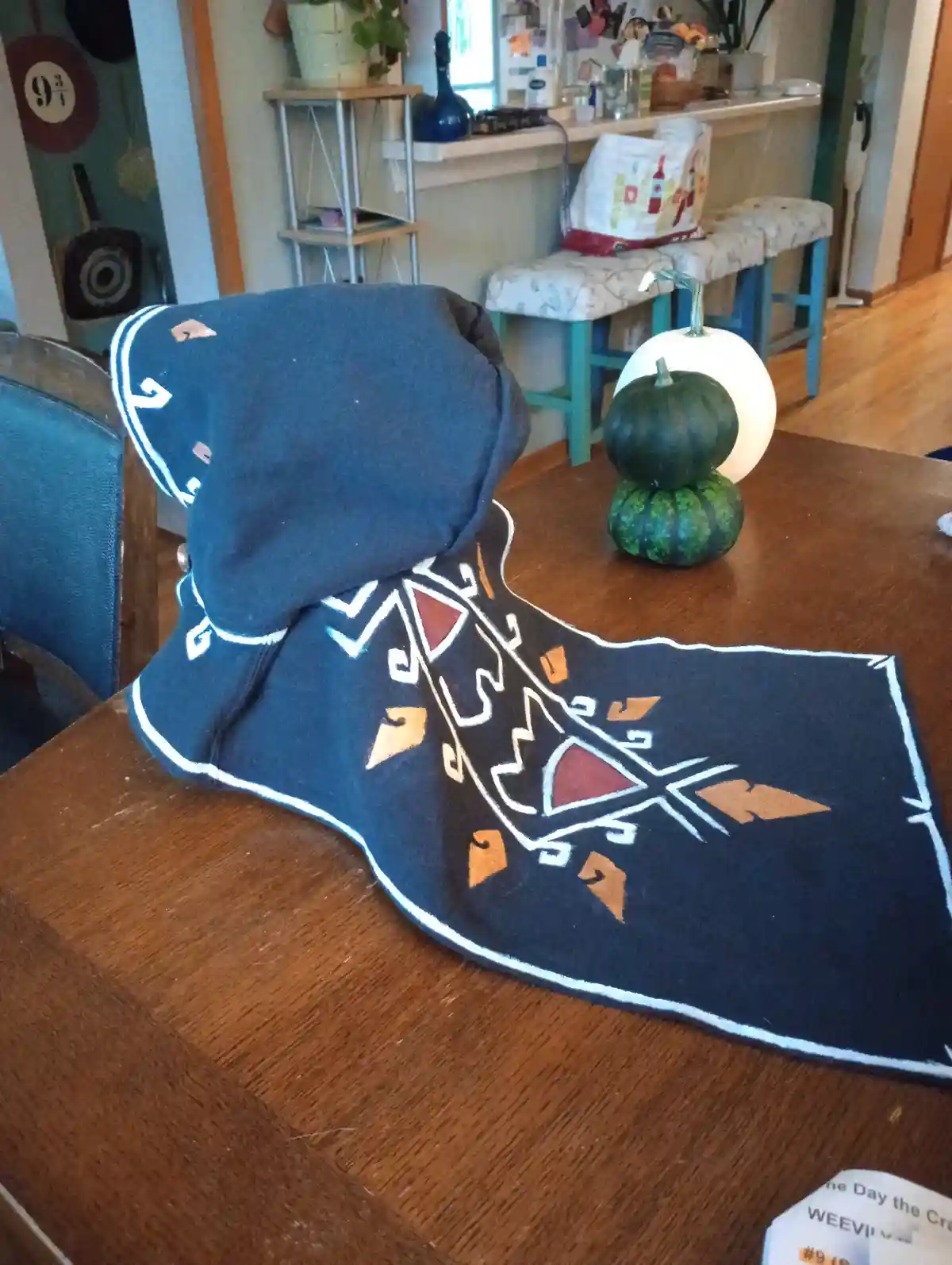 A dark blue blanket with geometric patterns in white and orange is draped over a wooden table, resembling a cape or cloak…