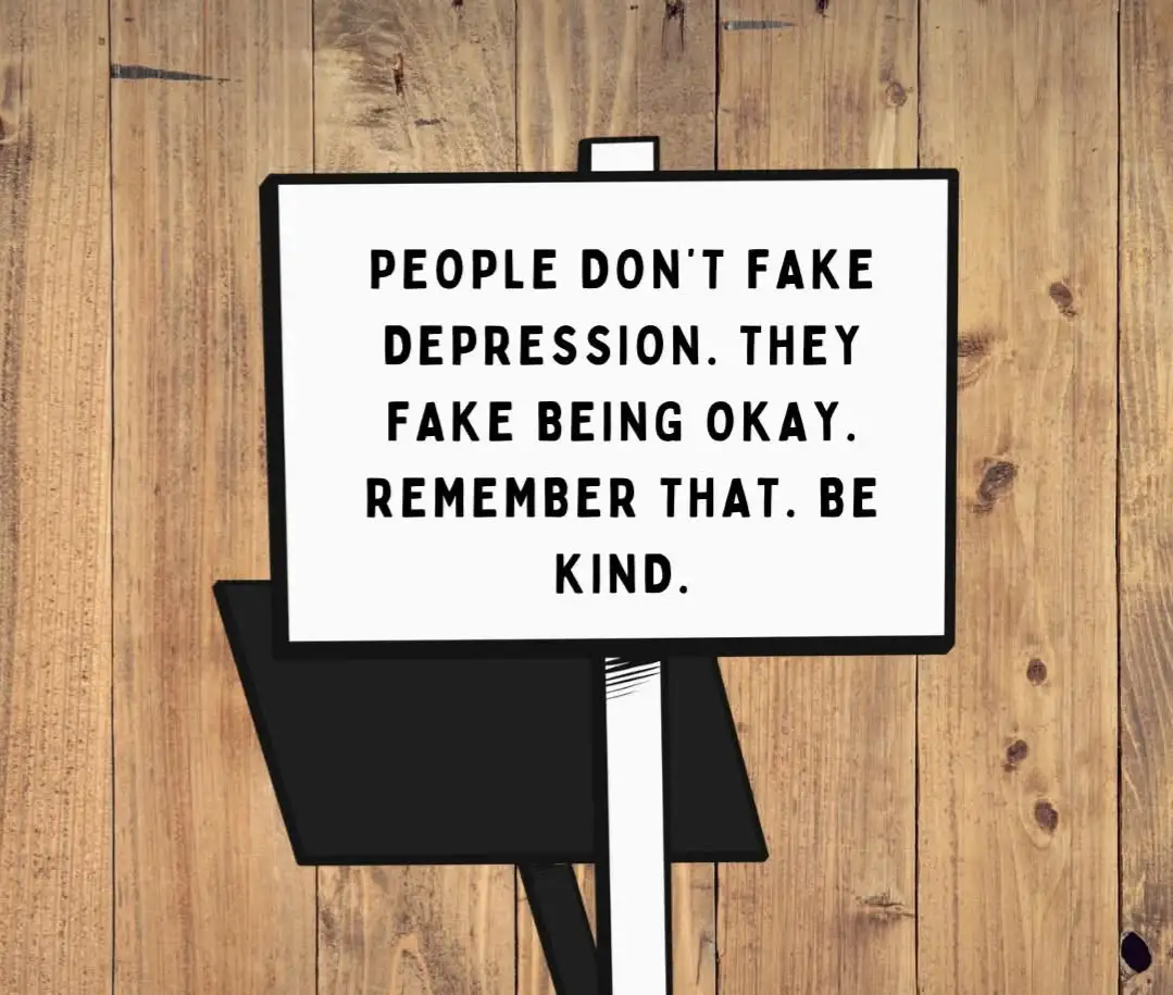 A white rectangular sign with black text is mounted on a black easel against a wooden plank background. The text reads…