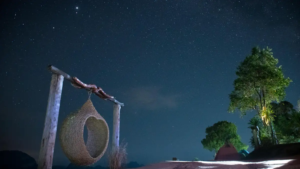 A velvety blackness is pierced by a thousand twinkling diamonds, as the night sky stretches above a lone, suspended rattan…