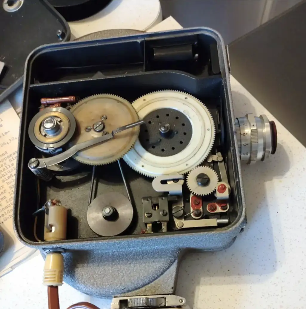 A close-up photo shows the open, internal mechanical components of an old, grey portable device, revealing gears, levers…