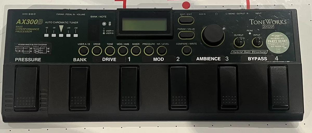 A close-up photo of a black Korg AX300B bass processor pedal with various knobs, buttons, and footswitches labeled…