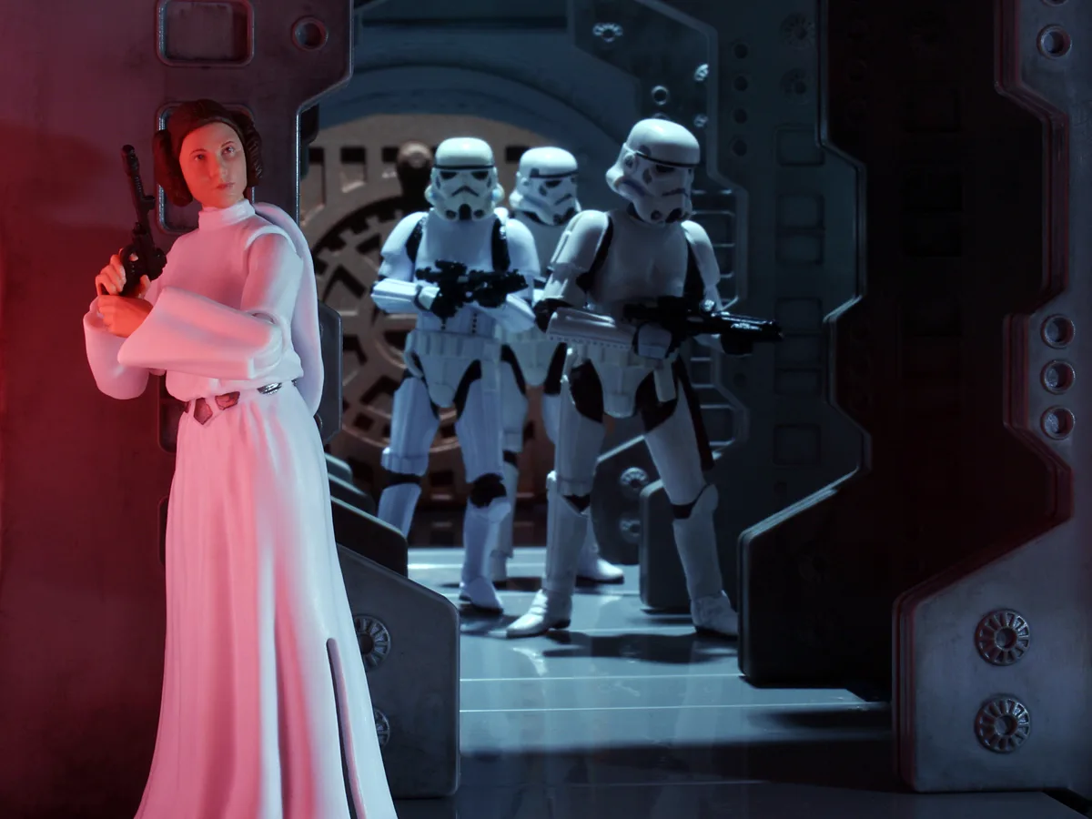 A Star Wars action figure of Princess Leia stands in a doorway, holding a blaster, as three Stormtrooper figures advance…