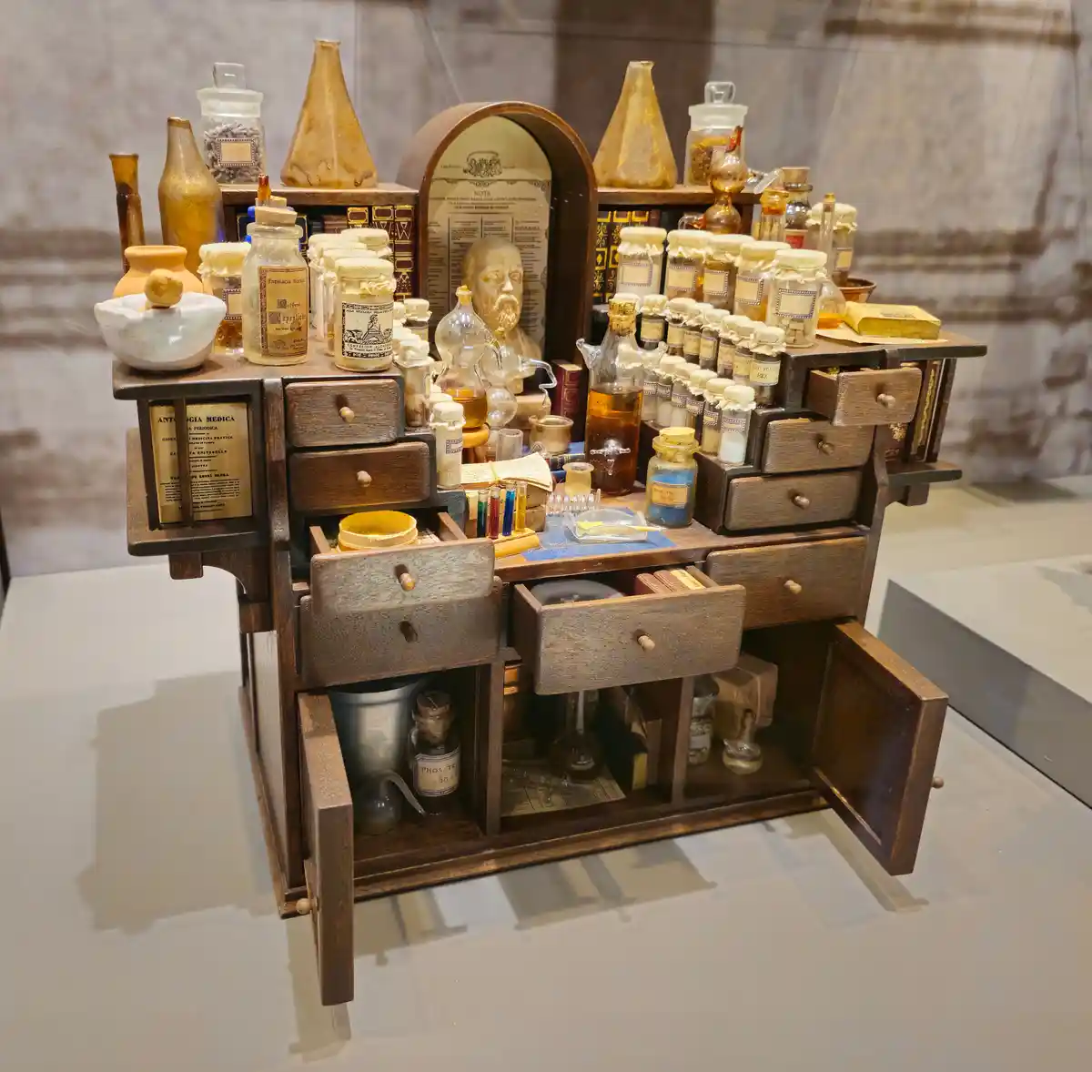 A detailed wooden apothecary cabinet with numerous drawers, some open, revealing various glass jars, bottles, and containers…