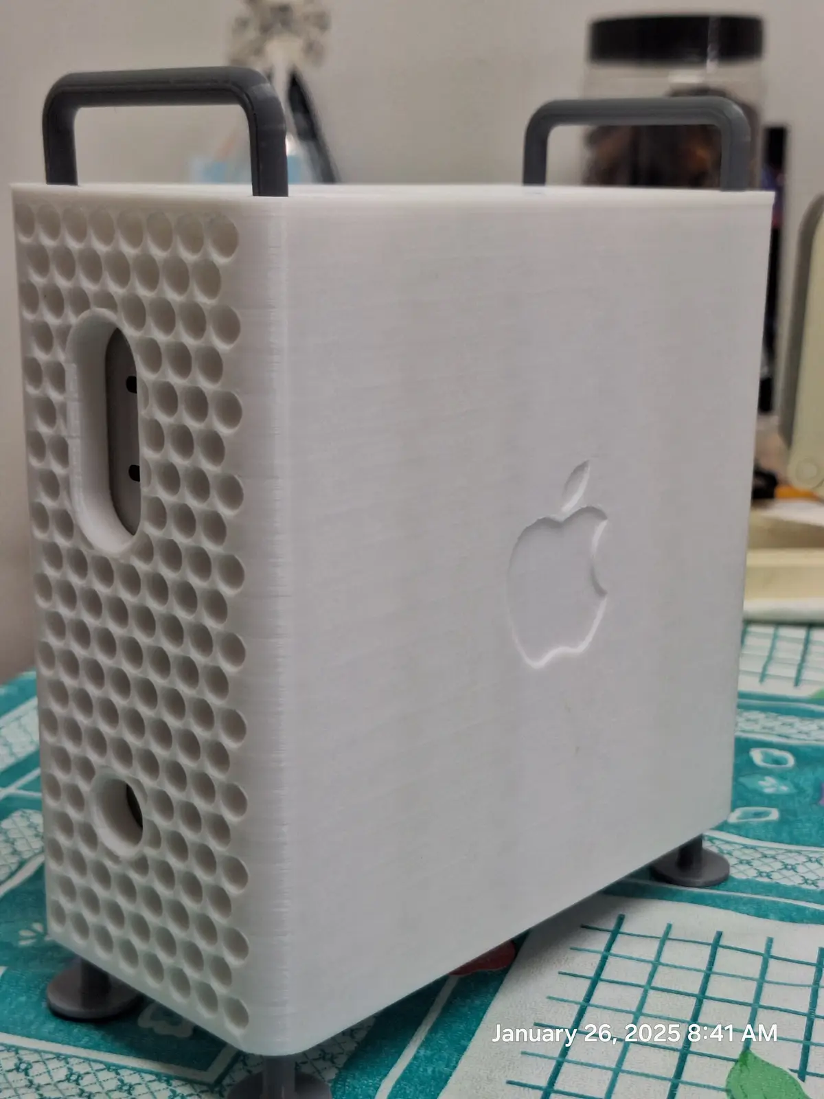 A white 3D-printed replica of an Apple Mac computer case, featuring a raised Apple logo, perforated side panels, and black…
