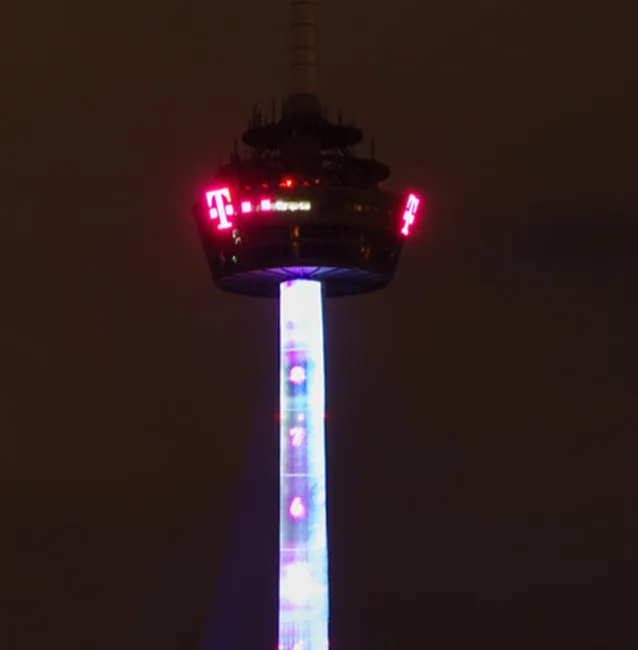 A tall tower at night with red digital displays on top showing the number '4' and the T-Mobile logo, and a vertical light…