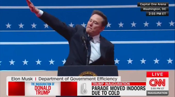 A man in a dark suit stands at a podium with a presidential seal, raising his right arm in a gesture resembling a political…