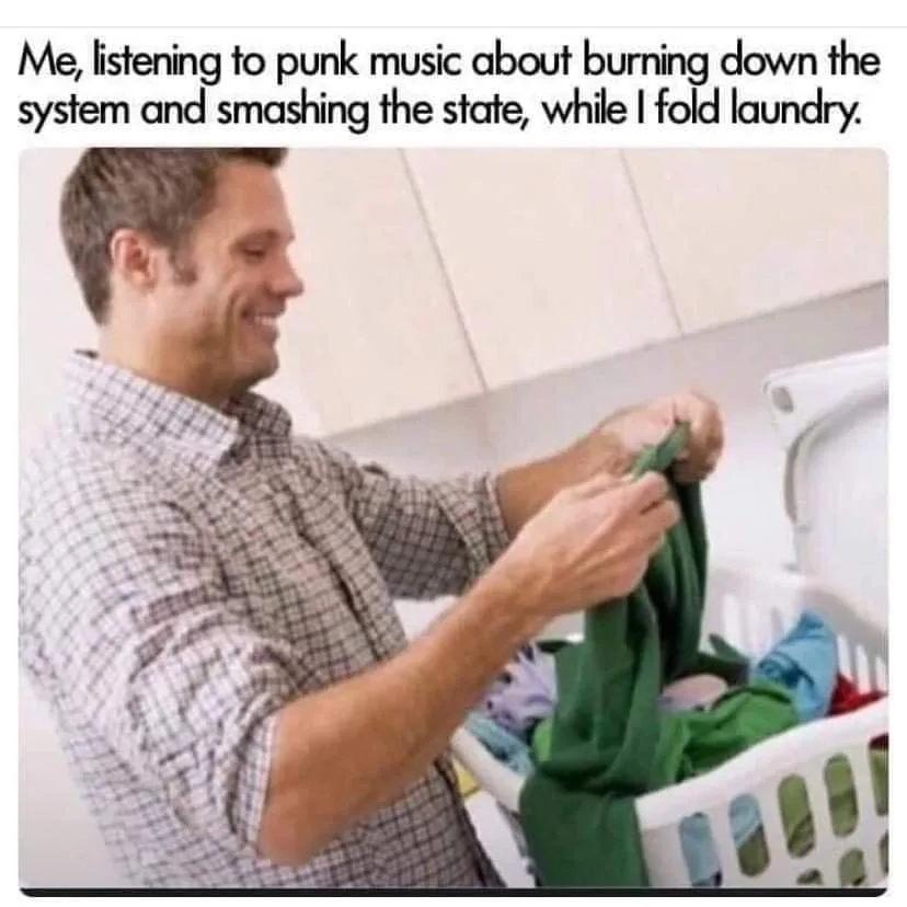 A man in a plaid shirt is smiling while folding laundry in a white basket. The overlaid text reads: 'Me, listening to punk…