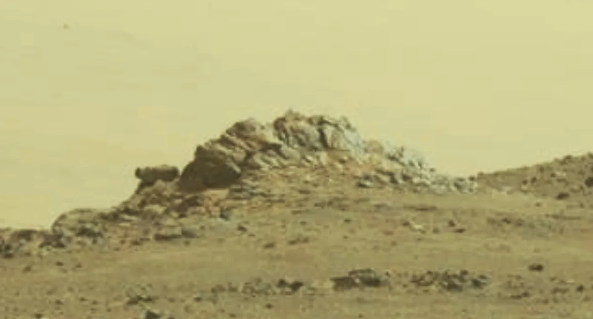 a blurry, sepia-toned image of a rocky outcrop on a barren, dusty planet surface under a hazy sky. The overlaid text reads…