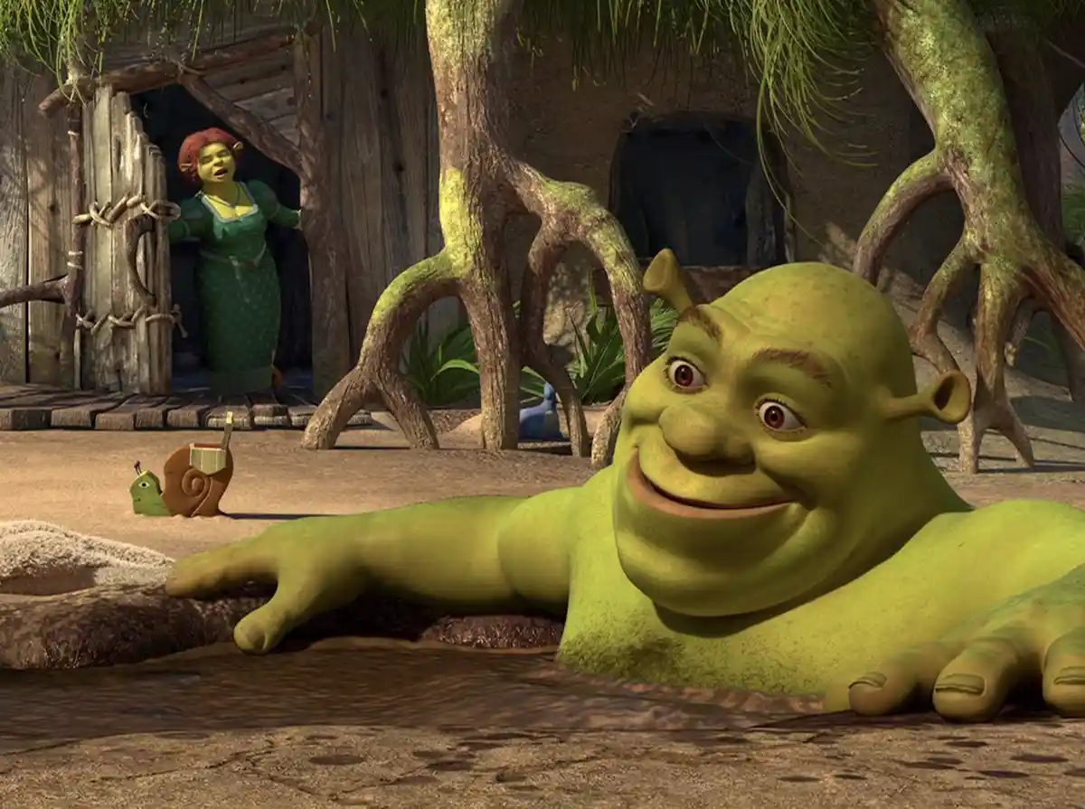A green ogre, Shrek, lies happily in a muddy puddle with a wide, smug grin, while his wife Fiona stands in the doorway of…