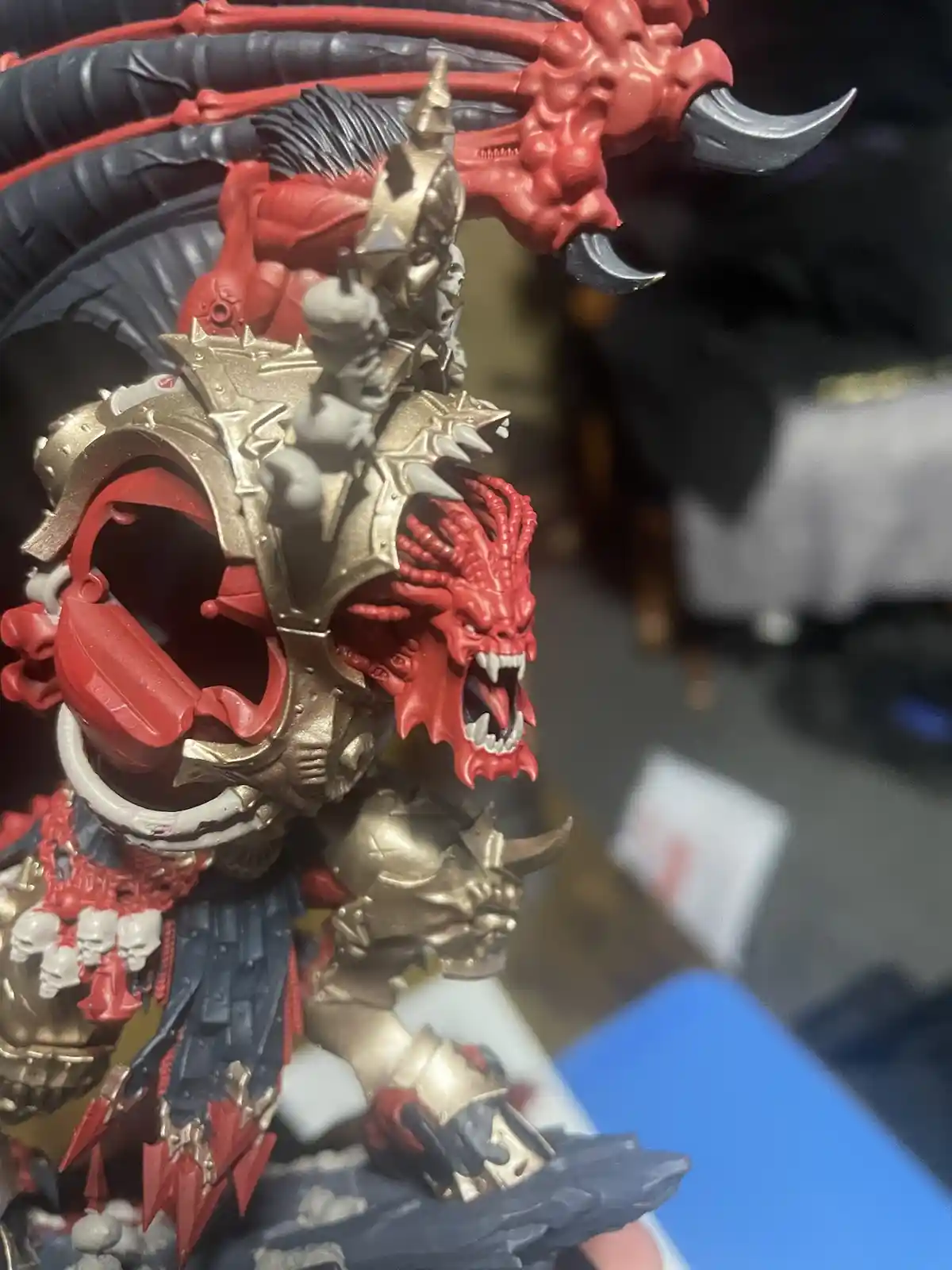 A close-up photo of a highly detailed, red and gold fantasy miniature figure with demonic features, including multiple…