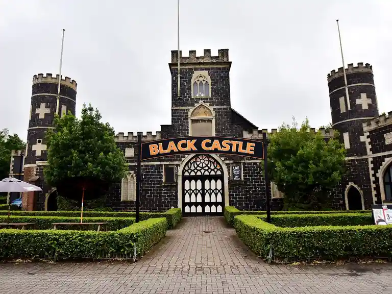 A photo of the Black Castle entertainment complex, a black stone building with turrets and a large arched gate. A black sign…
