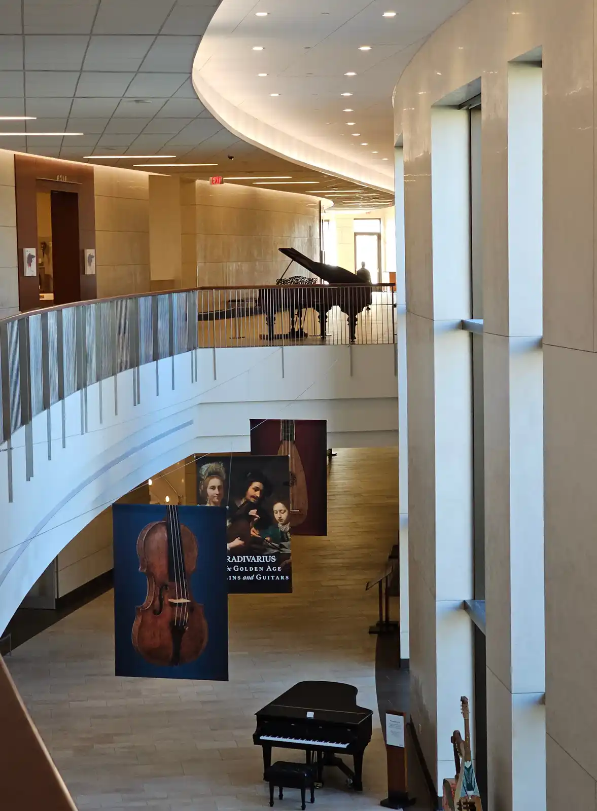 An interior shot of a modern museum atrium with curved architecture, featuring grand pianos on multiple levels and large…