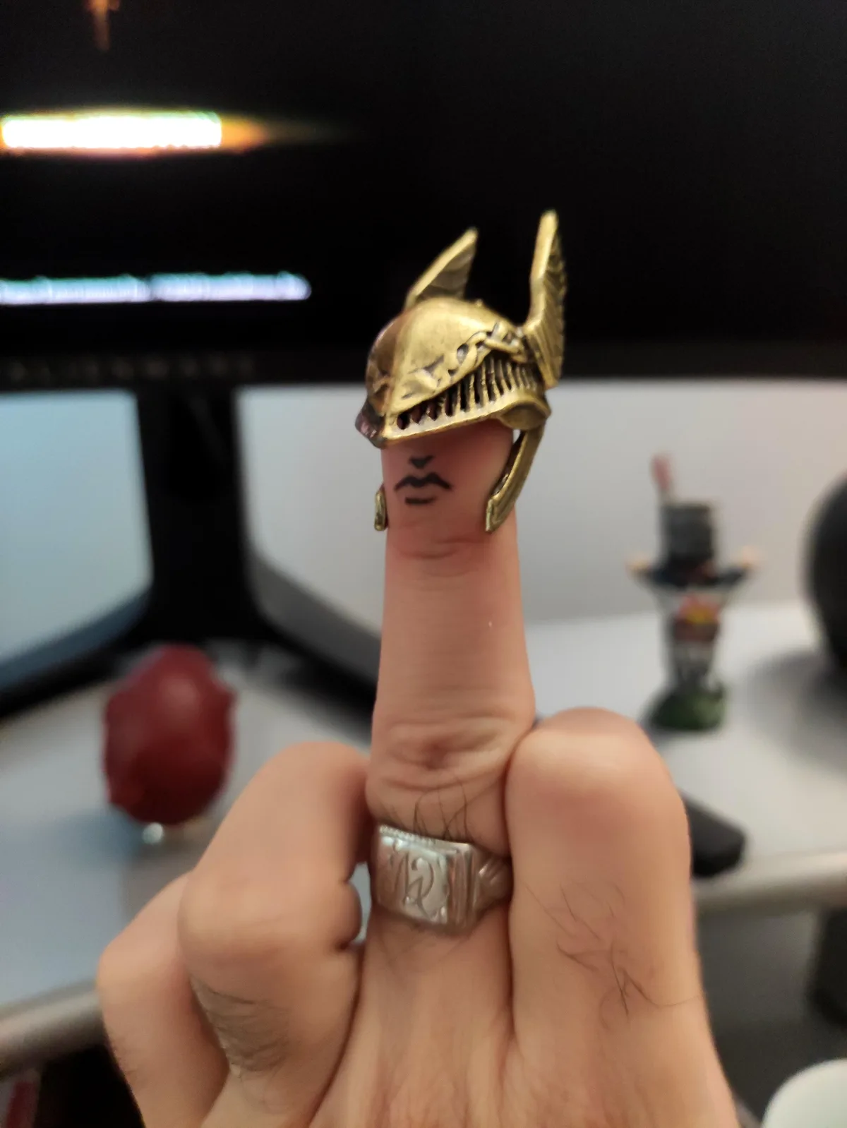 A close-up photo shows a person's finger extended, adorned with a gold-colored ring shaped like a stylized, menacing fish or…