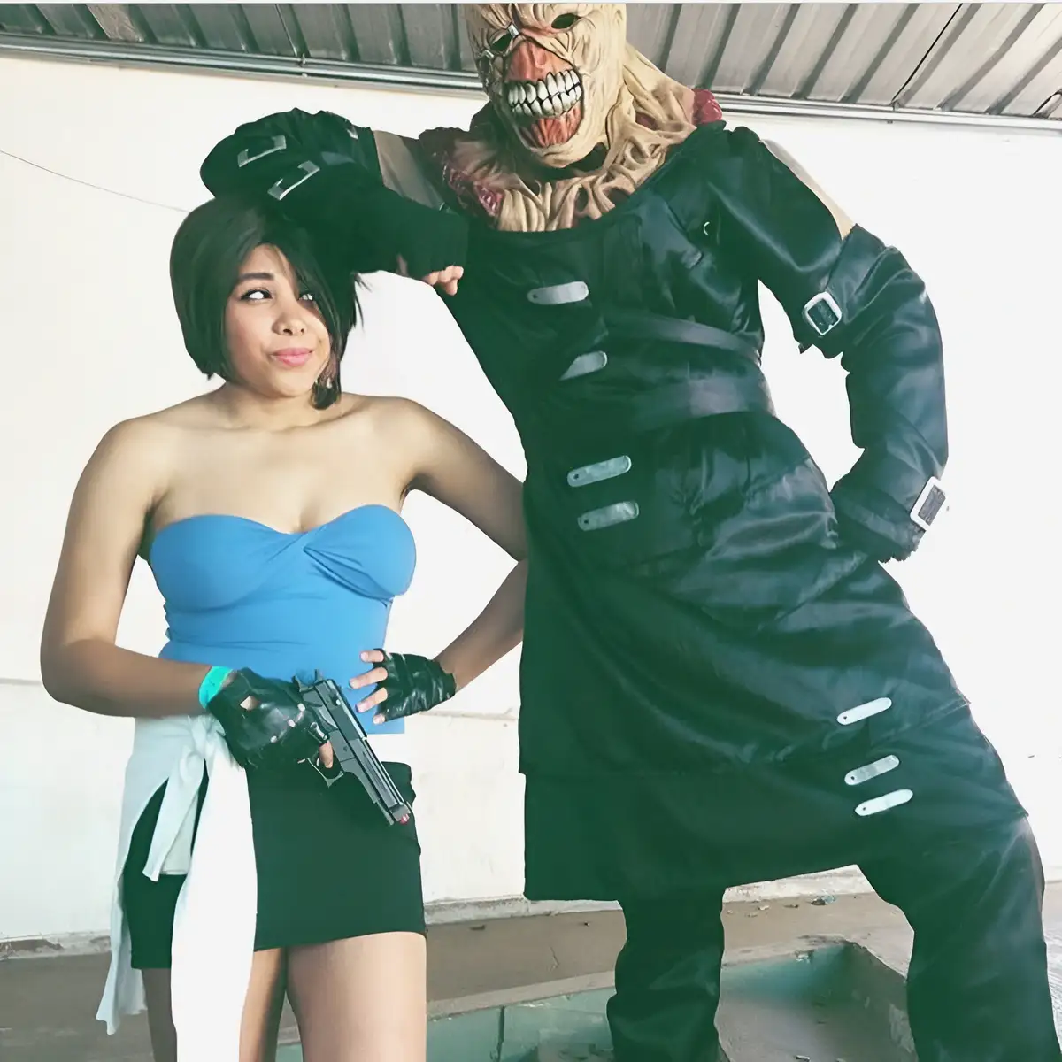A woman in a blue strapless top and black skirt holds a handgun while looking away with a smug expression, standing next to…