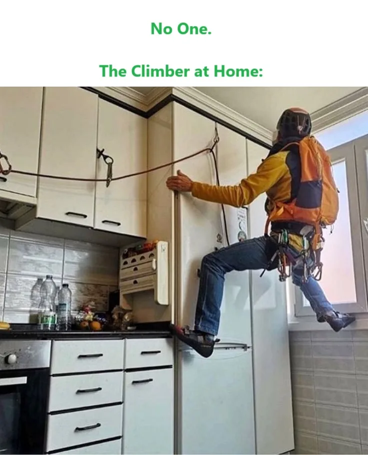 A person wearing full rock climbing gear, including helmet, harness, and rope, is scaling a kitchen cabinet while standing…
