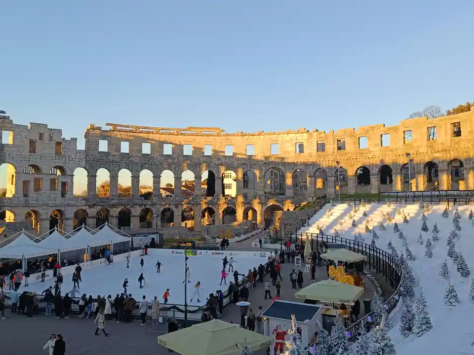 An ice skating rink is set up inside the ancient Roman amphitheater in Pula, Croatia, with people skating and spectators…