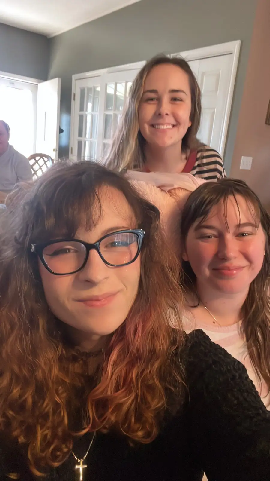 Three young women are in a selfie, with the person in front wearing glasses and a cross necklace, and the two behind her…