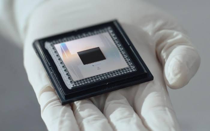 a gloved hand holds a square semiconductor chip with a black center and metallic grid, overlaid with the text 'this is the…