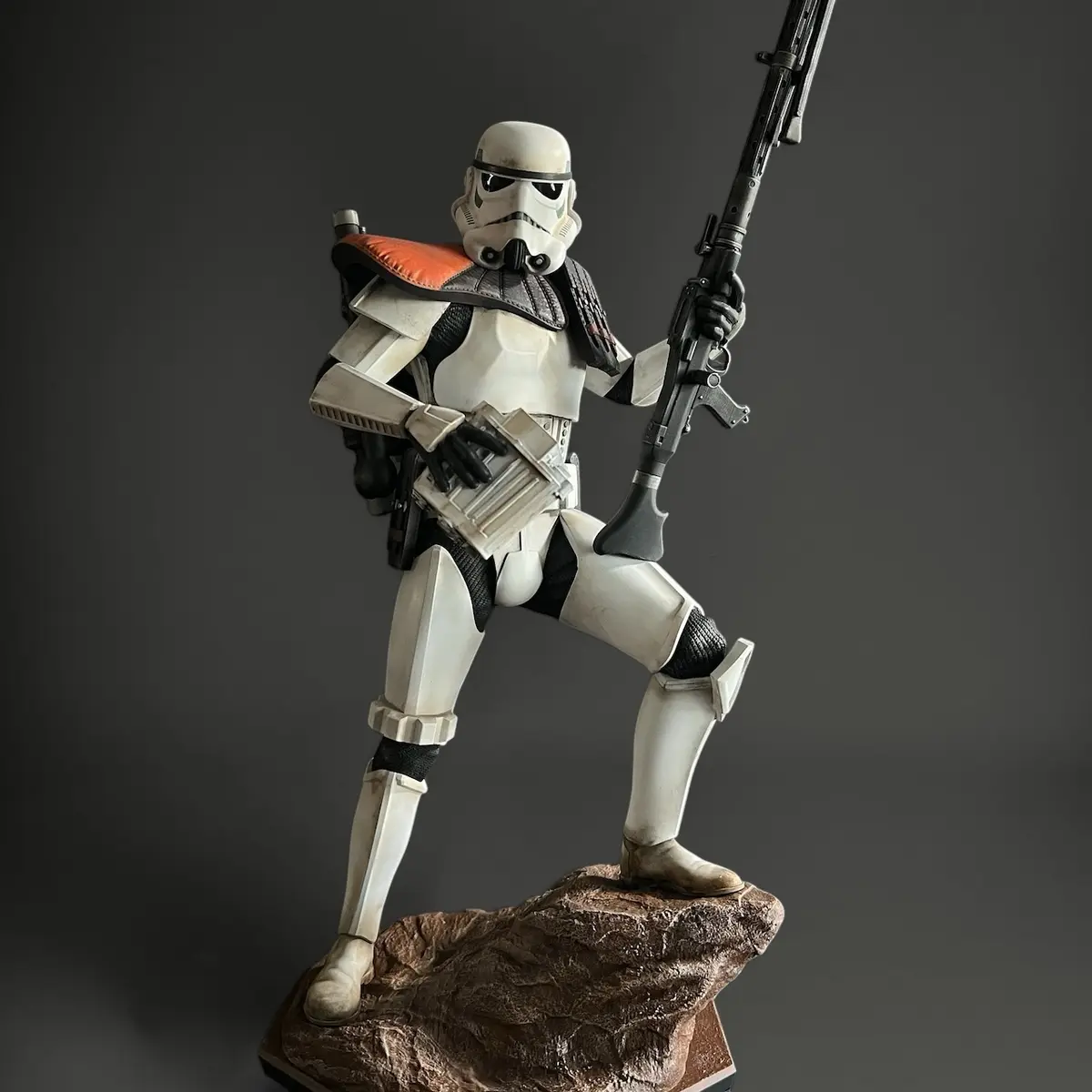 A detailed figurine of a stormtrooper from Star Wars, standing on a rocky base, holding a blaster rifle and a magazine. The…