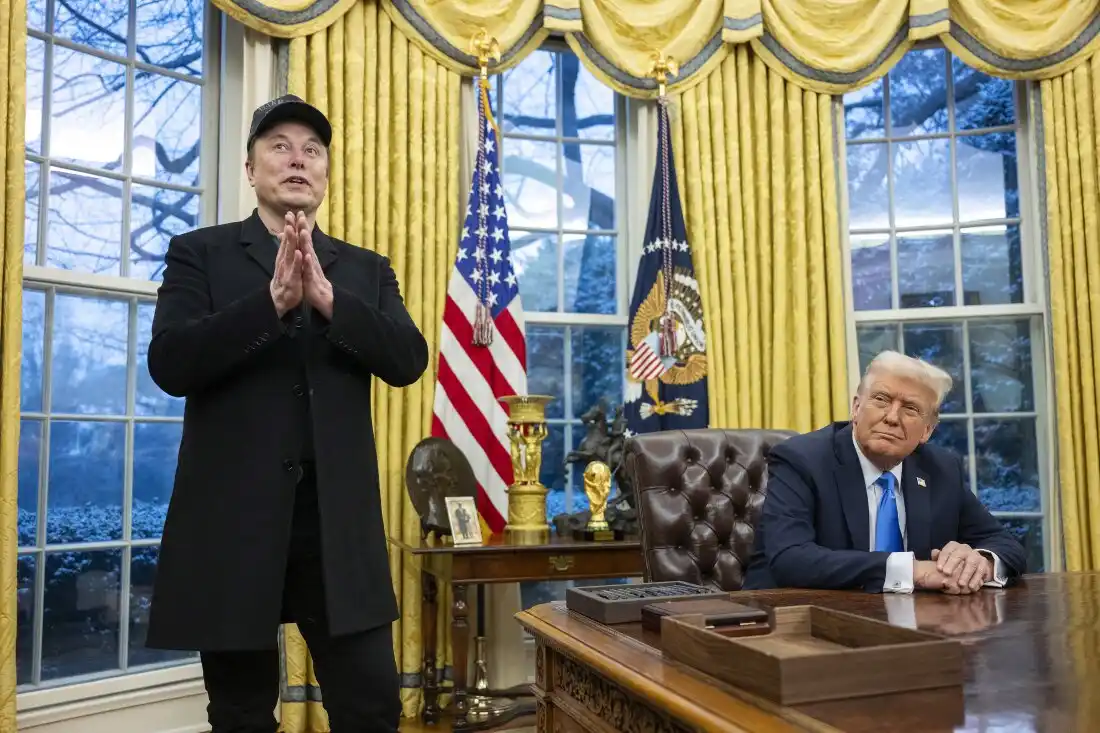 En una imagen de la oficina oval, Elon Musk, con gorra y abrigo negro, se pone de pie con las manos juntas en una postura de…