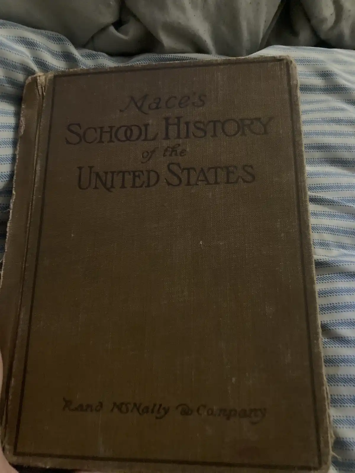 A close-up of a worn, brown cloth-bound textbook titled 'Mace's School History of the United States' by Rand McNally &…