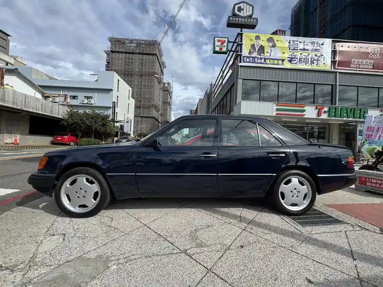 A dark blue Mercedes-Benz sedan is parked on a sidewalk in front of a 7-Eleven store with Chinese signage. The overlaid text…