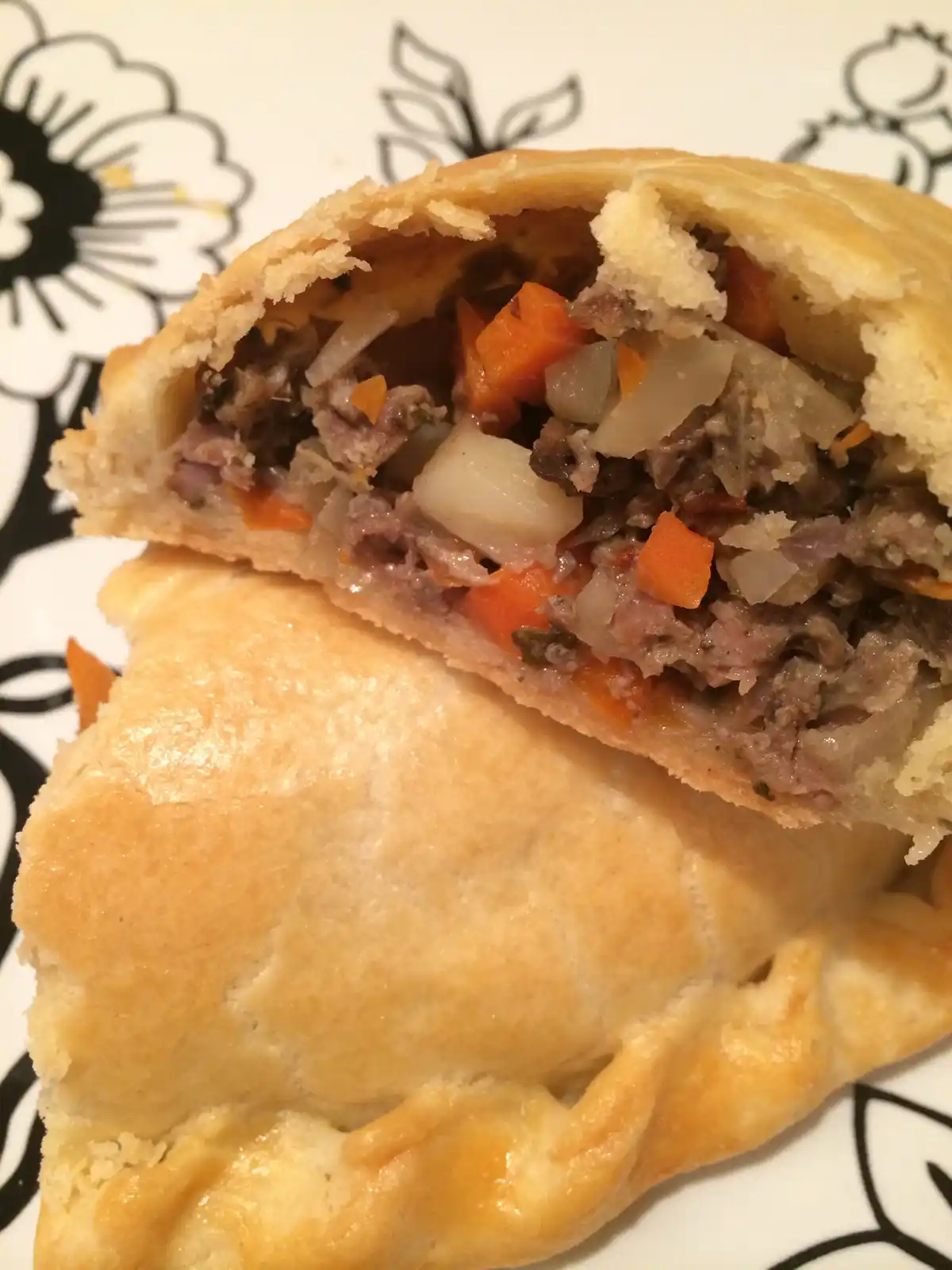 A close-up photo shows a golden-brown, flaky-crust meat pie that has been sliced open, revealing a filling of cooked meat…