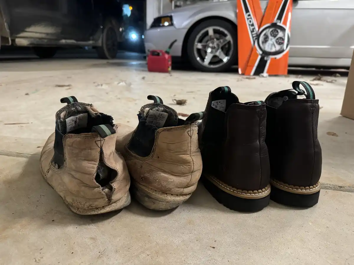 Two pairs of shoes sit side-by-side on a garage floor: one pair is visibly worn and torn, the other is new and pristine. In…