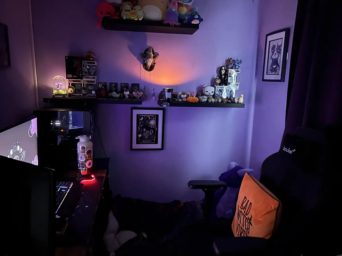 A dimly lit gaming room with purple ambient lighting, featuring shelves filled with Funko Pop figures, plushies, and…