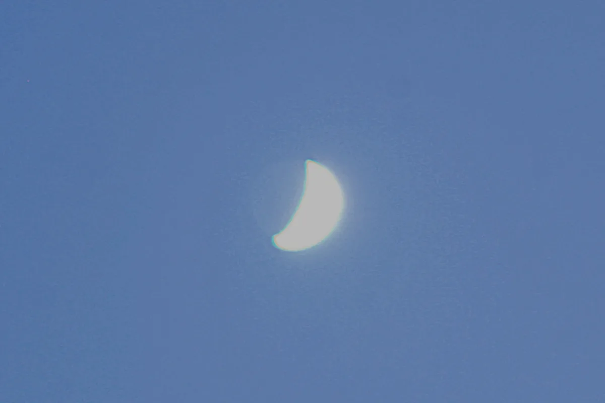 A crescent-shaped, glowing white object with a faint greenish halo is centered against a textured, solid blue background…