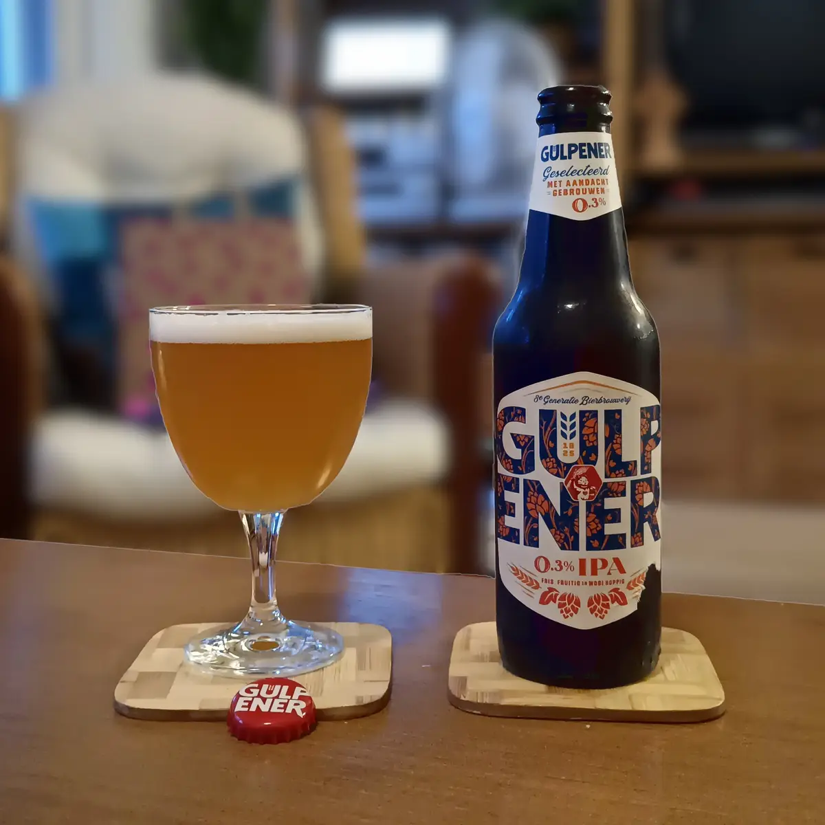 A dark blue bottle and a stemmed glass of Gulpener beer sit on wooden coasters on a wooden table, with the bottle's label…